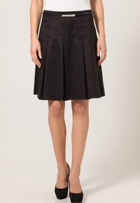 Zwarte geplooide rok van een gladde stof, beschikt over een aansluitende taille met een metallic accent aan de voorkant. De lengte valt boven de knie.