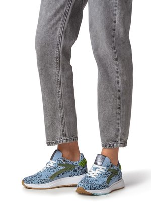 Baskets à motifs bleus avec des accents verts et des lacets blancs. Elles présentent une tige en tissu texturé et une semelle en caoutchouc. Portées avec un jean en denim gris.