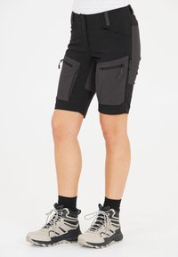 Svarta vandringsshorts med grå detaljer, som har flera fickor med dragkedja, en figurnära design och textilerad struktur. Kombinerat med lätta vandringskängor.