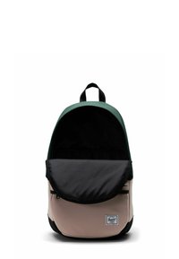 Sac à dos avec un dessus vert, un rabat noir et un corps beige. Forme arrondie, matériau en tissu, comporte une poche frontale et une étiquette avec le logo de la marque.