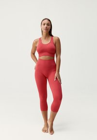 Červená sportovní souprava obsahující zkrácený top s kulatým výstřihem a ribbovým vzorem, doplněná úzkými legínami po lýtka.