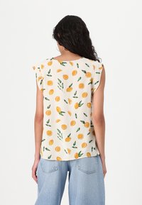 Krämfärgad kortärmad blus med ett livfullt mönster av orange och gröna löv. Lättviktsmaterial med avslappnad passform och mjuk textur.