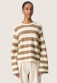 Strikket sweater i beige og brun, ribbet tekstur, rund hals, lange ærmer, afslappet pasform. Kombineret med lyse bukser.