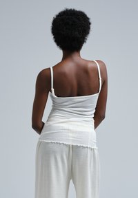 White tank top with thin straps and a gently gathered design, paired with matching loose pants featuring a scalloped hem. Soft, textured fabric.