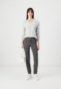 Grey fitted jeans paired with a light grey sweater and white sneakers, holding a small white handbag. Simple design and casual style.