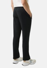 Czarne spodnie dresowe wykonane z miękkiego materiału, wyposażone w zapinaną na suwak tylną kieszeń, boczne kieszenie oraz zwężany krój aż do kostki.