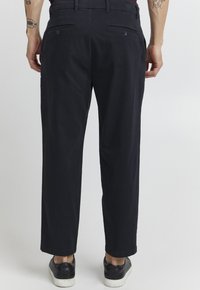 Pantalon marine en coupe décontractée avec une texture en coton lisse, doté de deux poches arrière et d'un devant plat, associé à des baskets noires.