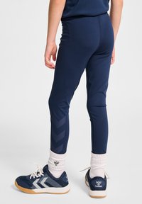 Granatowe legginsy sportowe o gładkiej fakturze, z zygzakowatym wzorem w nieco ciemniejszym odcieniu wzdłuż zewnętrznych nogawek, w połączeniu z granatowymi sneakersami.