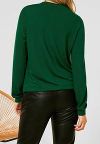 Vihreä, neuloksesta valmistettu pitkähihainen paita, jossa on rento istuvuus, pyöreä pääntie ja hienovaraiset sauma-yksityiskohdat, yhdistetty mustiin nahkahousuihin.