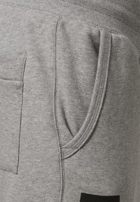 Grå sweatshirtbyxor gjorda av mjukt tyg, med en sidoficka, elastisk midja och framträdande s ömnadsdetaljer.