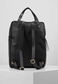 Zwarte leren rugzak met een gestructureerd oppervlak, voorzien van twee verstelbare schouderbanden en een bovenhandgreep, tentoongesteld op een witte standaard tegen een effen achtergrond.