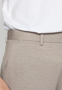 Pantaloni bej deschis, croiți, dintr-un material texturat. Au un front plat, un croi slim și cusături subtile pe talie.