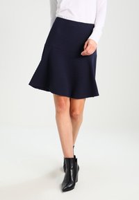 Gonna svasata A-line blu navy con tessuto testurizzato, con vita aderente e orlo a ginocchio. Abbinata a stivaletti neri fino alla caviglia.