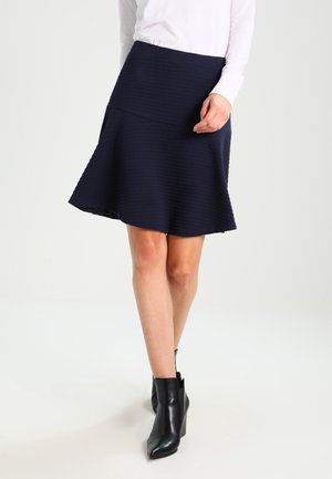 Jupe évasée A-line bleu marine en tissu texturé, dotée d'une taille ajustée et d'un ourlet au niveau du genou. Associée à des bottines noires.