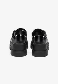 Black platform sandals with smooth synthetic material, adjustable buckle, open back, and textured sole for grip. Minimalist design.