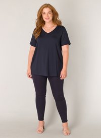 Navy V-hals top gemaakt van zachte stof, gecombineerd met aansluitende navy leggings. Het model draagt strap sandalen in beige en toont een ontspannen pasvorm.