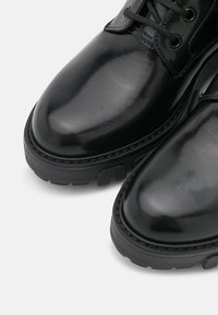 Zbliżenie na wypolerowane czarne skórzane buty z grubymi gumowymi podeszwami i czarnymi sznurowadłami na białym tle.