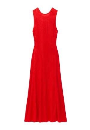 Joven mujer con cabello largo y rizado, que lleva un vestido sin mangas rojo acanalado, collar de cuentas azules y sostiene un bolso beige tejido.