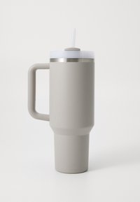 Reusable travel mug in soft beige, with a tapered body, sturdy handle, white lid, and straw. Smooth texture with metal accent near the lid.