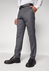 Pantalons gris sur mesure avec une coupe droite, dotés d'une texture lisse, de poches latérales, et associés à des chaussures en cuir noires et une ceinture.
