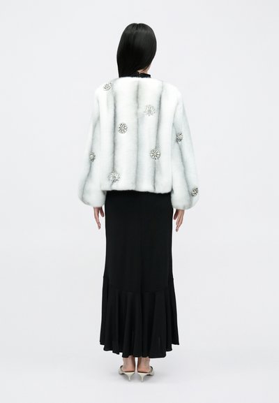 Valge kunstkarusnahast jakk hõbedaste lilleornamentidega, kombineeritud liibuva musta kleidi ja lehviva äärega, kantud teravate kontsadega.