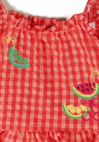 Tissu vichy rouge et rose avec détail de vêtement froncé, orné d’un motif brodé de cosses de petits pois vertes, tranche de pastèque, quartier de citron et cerises.