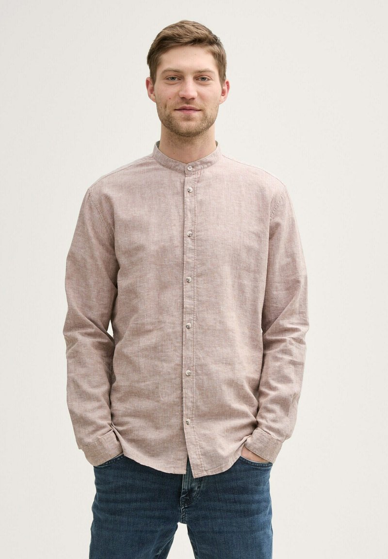 Camisa de botones rosa claro con cuello mao, mangas largas y tejido texturizado. Lleva puesta con unos vaqueros oscuros.