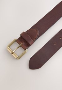 Brown leather belt with a gold metal buckle. Smooth texture, pointed end, and four punch holes for adjustment. Stitched accents near the buckle.