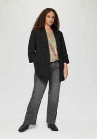 Schwarzer Blazer mit strukturierten Schultern, kombiniert mit einem grauen, metallischen Grafik-T-Shirt mit rundem Design und dunkelblauen, geraden Jeans.