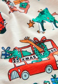 Tissu coloré présentant des animaux de dessin animé, un bus rouge et des cadeaux de Noël. Le design inclut un dinosaure vert et des éléments festifs comme une couronne.