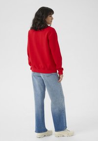 Rotes Sweatshirt mit langen Ärmeln, Rundhalsausschnitt und gerippten Bündchen, kombiniert mit hellblauen, geraden Jeans und beigen, klobigen Sneakern.