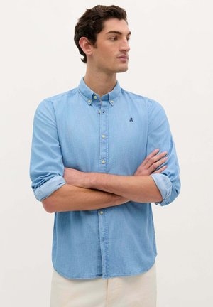 Cămașă button-up de un albastru deschis, cu mâneci lungi răsucite la manșete. Prezintă un mic logo brodat pe piept. Material moale și texturat.