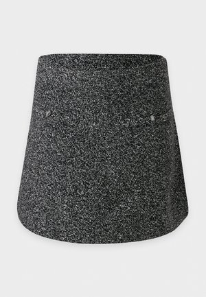 Une femme porte un pull noir à col roulé, une minijupe grise en tweed, des bottes noires montantes jusqu’aux genoux et un sac à bandoulière marron, sur un fond blanc uni.