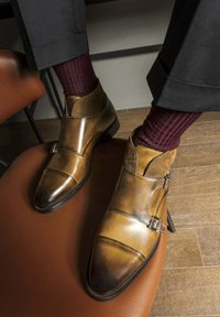 Bottines en cuir marron avec doubles boucles, bout pointu et un mélange de textures vernies et en daim. Portées avec des chaussettes côtelées bordeaux.