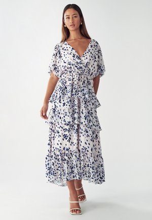 Maxi dress in lightweight fabric features a V-neck, tiered ruffles, and a blue dot pattern on a light background. Accented with short sleeves.