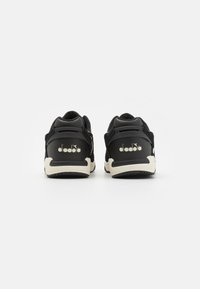 Black sneakers featuring suede and mesh material, round shape, white sole, with textured accents and logo detail on the heel.