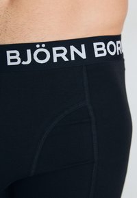 Fekete boxer alsónadrág széles fekete derékpánttal, amelyen fehér betűkkel áll "BJÖRN BORG". Simán tapintású, testhezálló kialakítás elülső zsebbel.