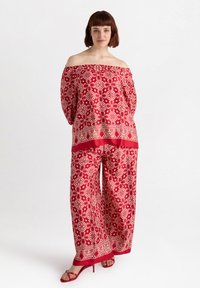 Top rosso senza spalle e pantaloni a gamba larga con motivo floreale e un design a bordo contrastante. Il tessuto appare leggero e dalla consistenza liscia.