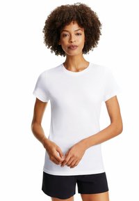 Weißes Baumwoll-T-Shirt mit kurzen Ärmeln und rundem Halsausschnitt, das eine glatte Textur und eine lockere Passform aufweist. Getragen mit schwarzen Shorts.