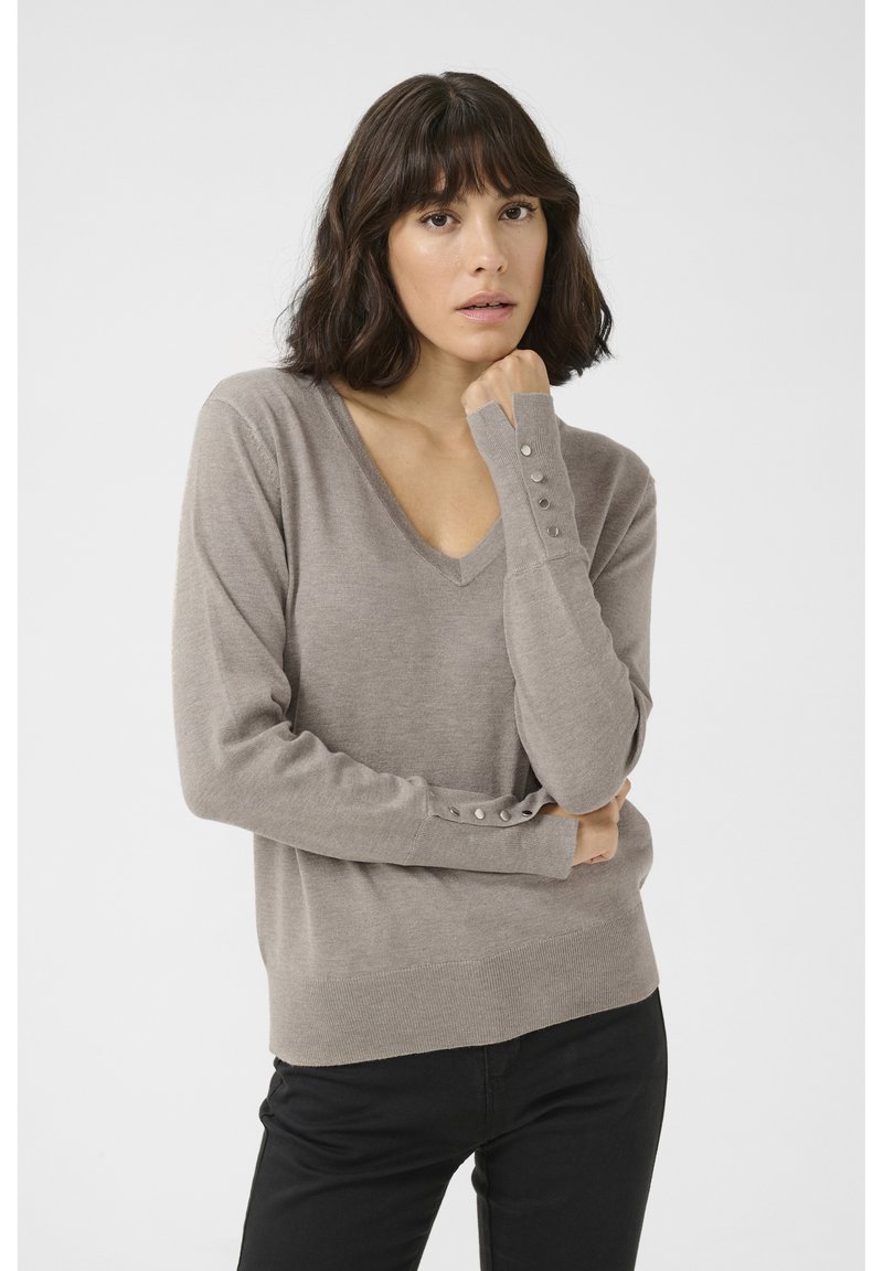 Maglione beige chiaro a V con maniche lunghe, dotato di dettagli a bottoni sui polsi. Texture liscia e vestibilità leggermente ampia, progettato per il comfort.