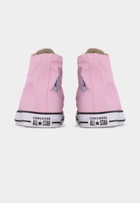 Ζευγάρι ροζ ψηλές αθλητικές κάλτσες Converse All Star, εμφανιζόμενες από πίσω, απεικονίζοντας τις λευκές καουτσούκ σόλες με μαύρες ρίγες και λογότυπο.