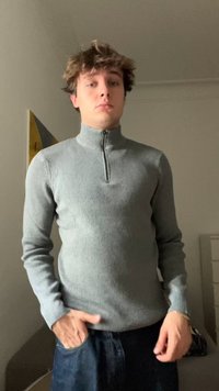 Sivý rebrovaný tričko s dlhým rukávom a vysokým golierom s polovičným zipsom. Model stojí s rukami vo vreckách džínov. Jednoduchý, priliehavý štýl.