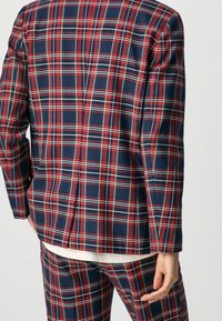 Giacca a quadri con colori rosso, blu navy e bianco, realizzata in tessuto testurizzato, con uno spacco posteriore singolo e maniche strutturate.