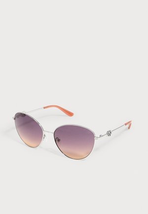 Lunettes de soleil à monture argentée avec des verres dégradés du violet à l’orange et des embouts orange translucides sur les fines branches métalliques reposant sur une surface blanche.