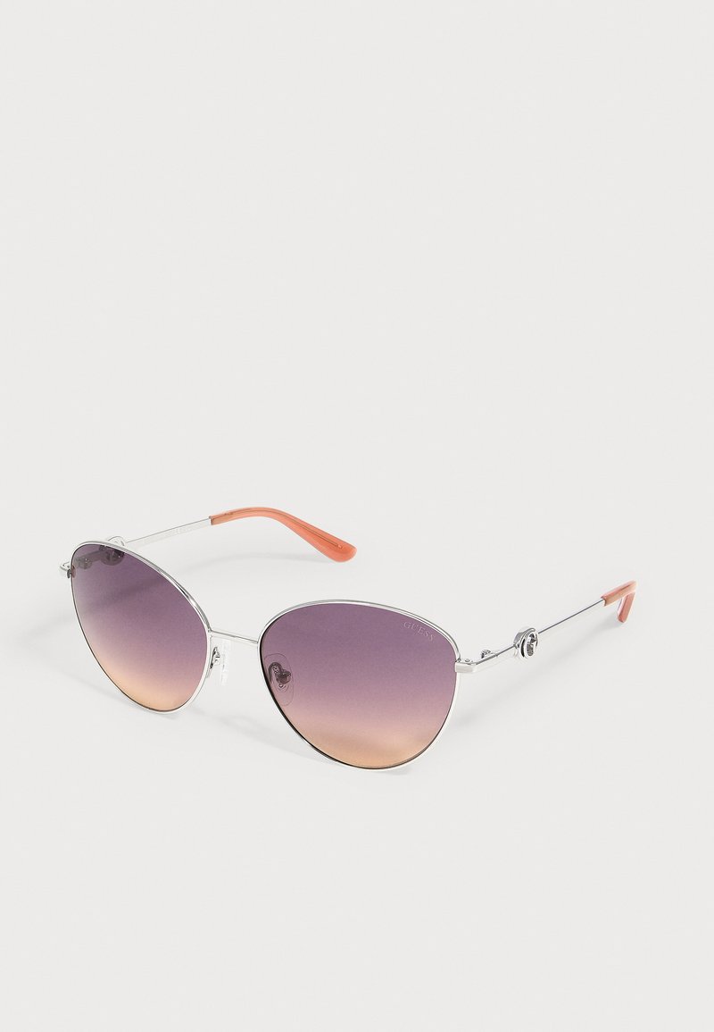Lunettes de soleil à monture argentée avec des verres dégradés du violet à l’orange et des embouts orange translucides sur les fines branches métalliques reposant sur une surface blanche.
