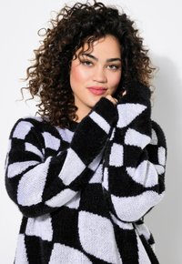 Maglione a scacchi bianco e nero con una texture pelosa, caratterizzato da maniche lunghe e una vestibilità ampia, con un motivo di grandi quadrati.