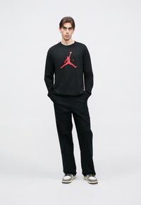 Μαύρο πουκάμισο με μακριά μανίκια και κόκκινο λογότυπο Jumpman, σε συνδυασμό με μαύρο παντελόνι και γκρι αθλητικά παπούτσια. Απλός σχεδιασμός, casual εφαρμογή και μονόχρωμα χρώματα.