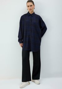 Marineblå ternet skjorte med knaplukning foran, afslappet pasform og lange ærmer, kombineret med sorte bukser med vide ben og hvide sneakers.