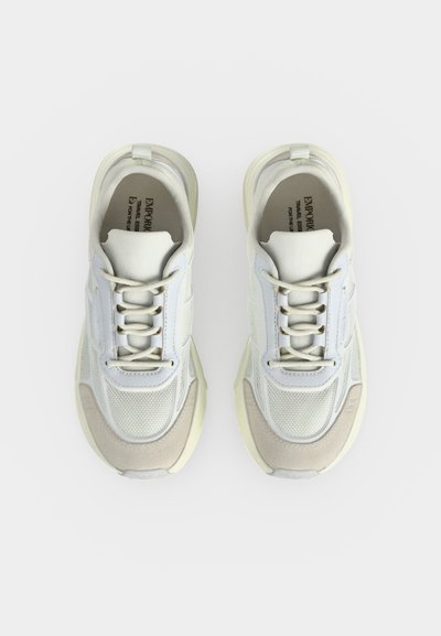 Paire de baskets blanches et beiges à lacets avec des détails en mesh et cuir vues de dessus sur un fond uni.