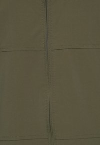 Gros plan d'un tissu vert olive avec une fermeture éclair verticale centrée et des coutures horizontales traversant la fermeture éclair.